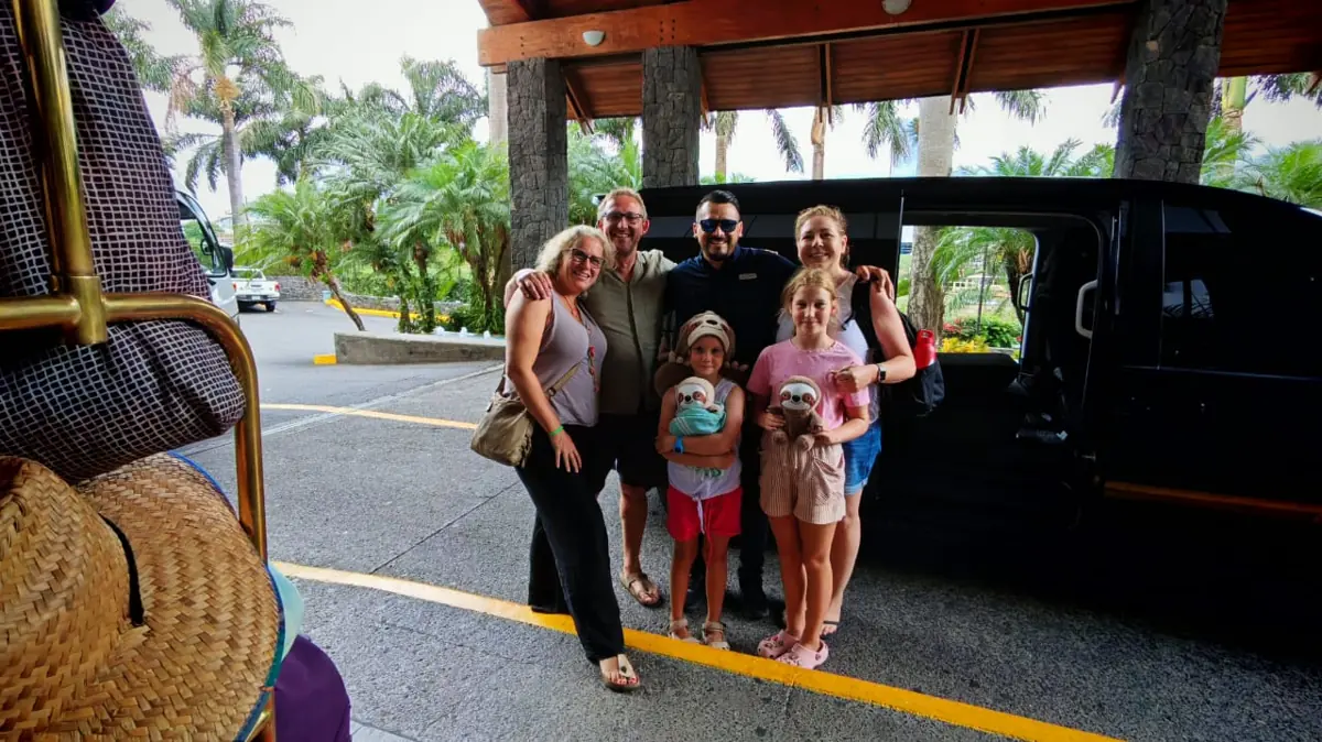 A family with two girls and their driver beside a black van at a hotel entrance