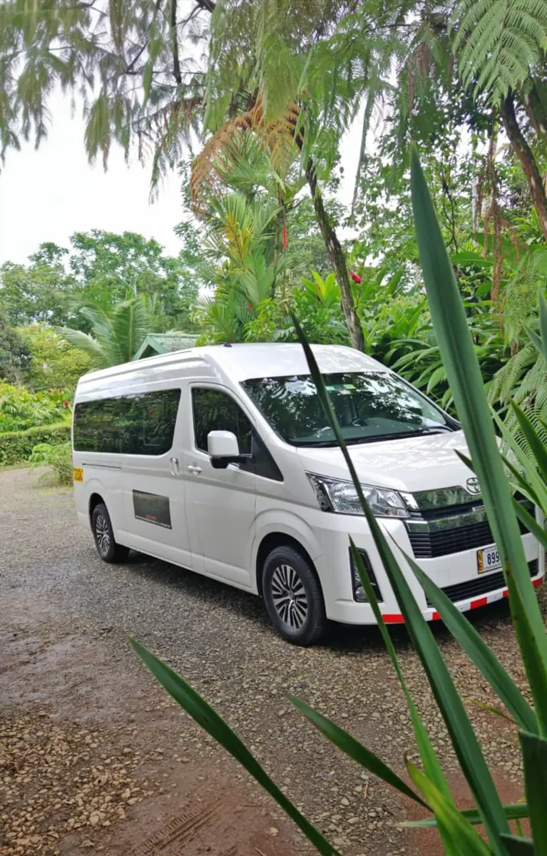 A white Toyota Hiace on a gravel drive among tropical plants