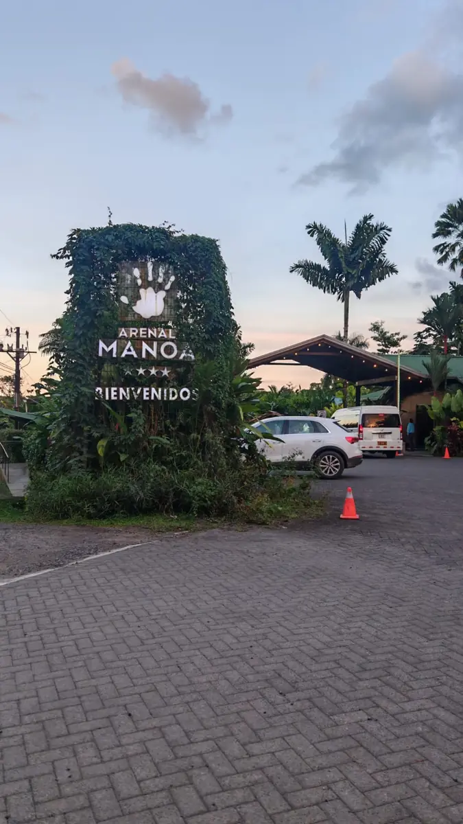 Welcome sign of Arenal Manoa covered in climbing plants