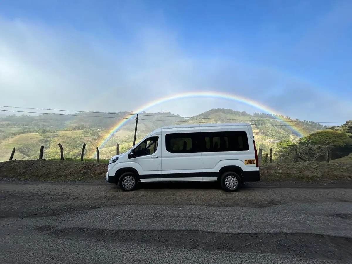 A white Tropical Experts van on a mountain road under a rainbow