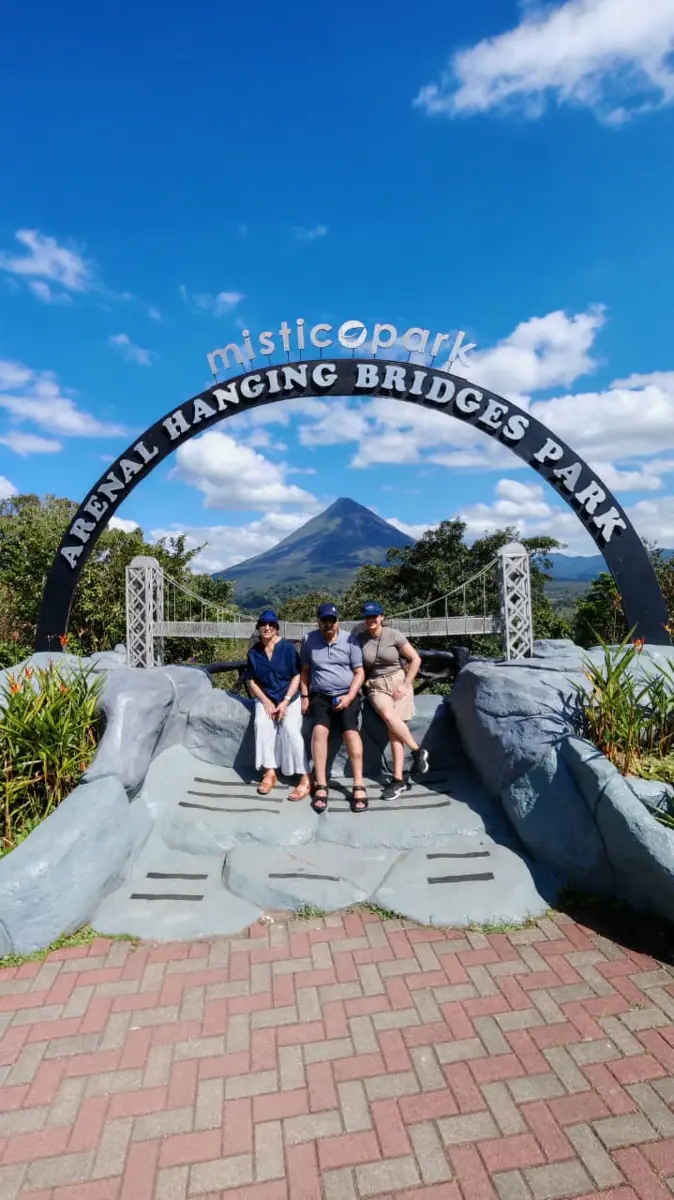 Travellers under the Místico Arenal Hanging Bridges Park arch, with Arenal volcano behind