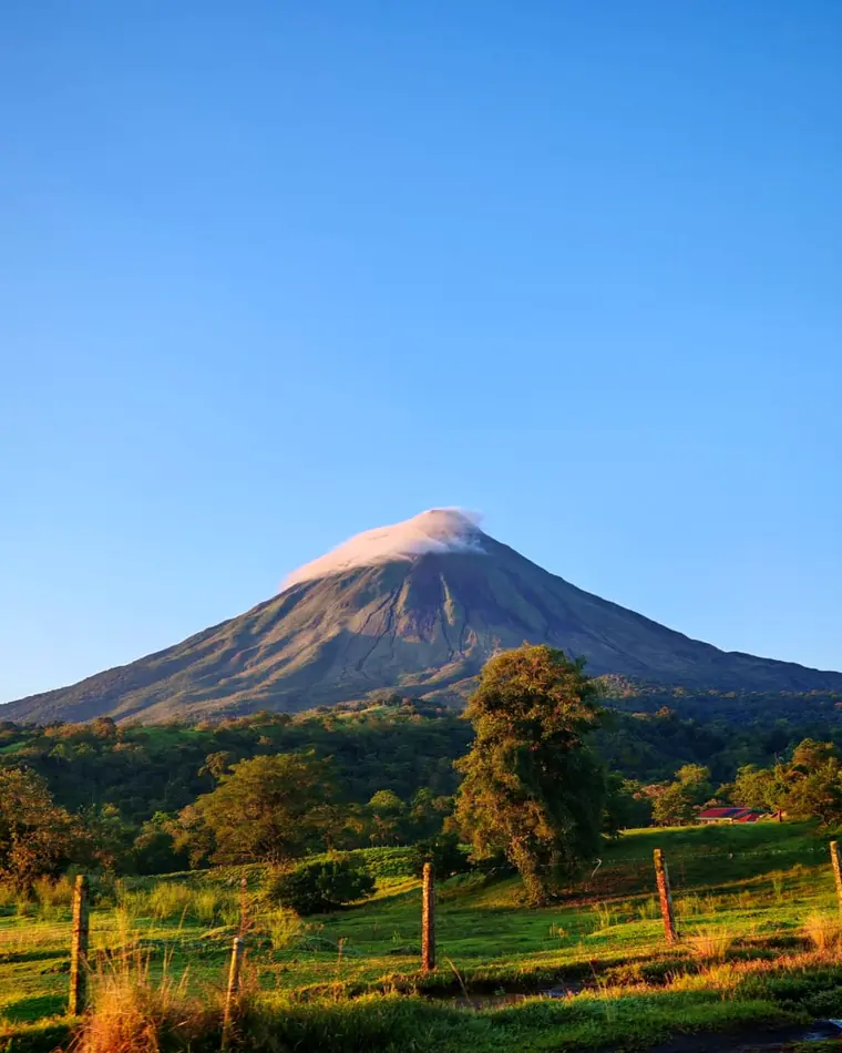 El volcán Arenal al amanecer con luz dorada sobre los potreros