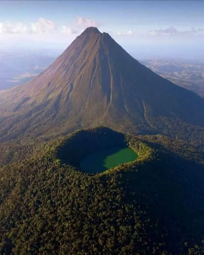 Vista aérea del cono del volcán Arenal con el cráter y una laguna verde en el bosque
