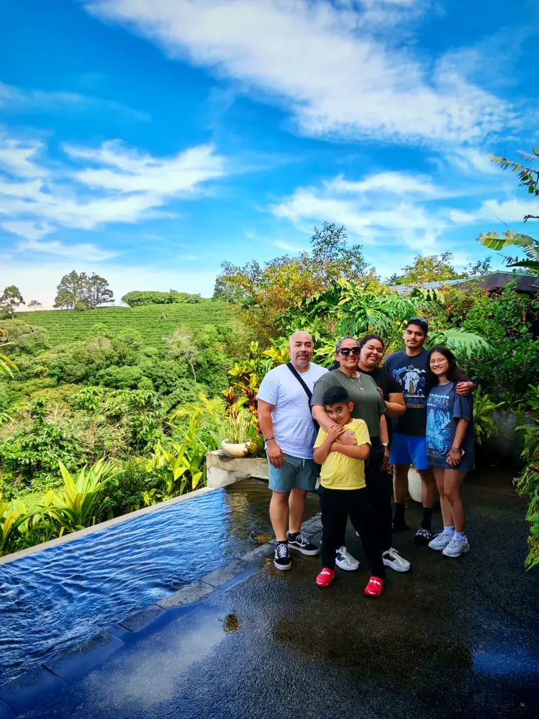 Familia de visitantes en una finca de café con el cafetal detrás