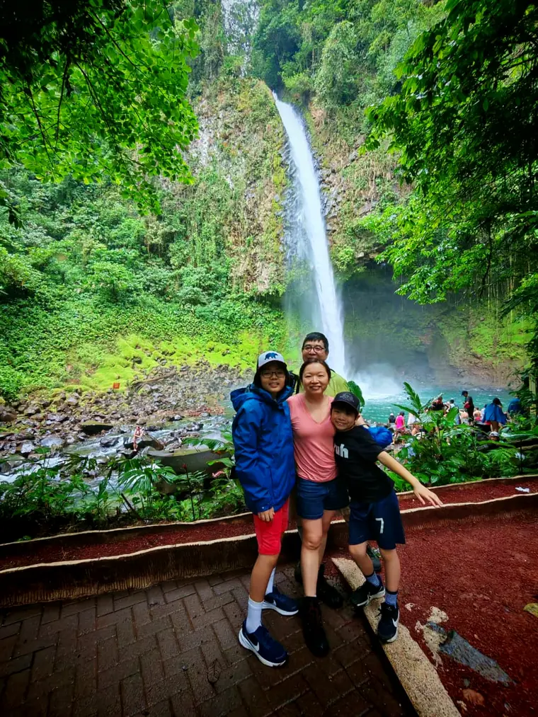 Familia frente a la catarata de La Fortuna con el caudal alto de la temporada verde