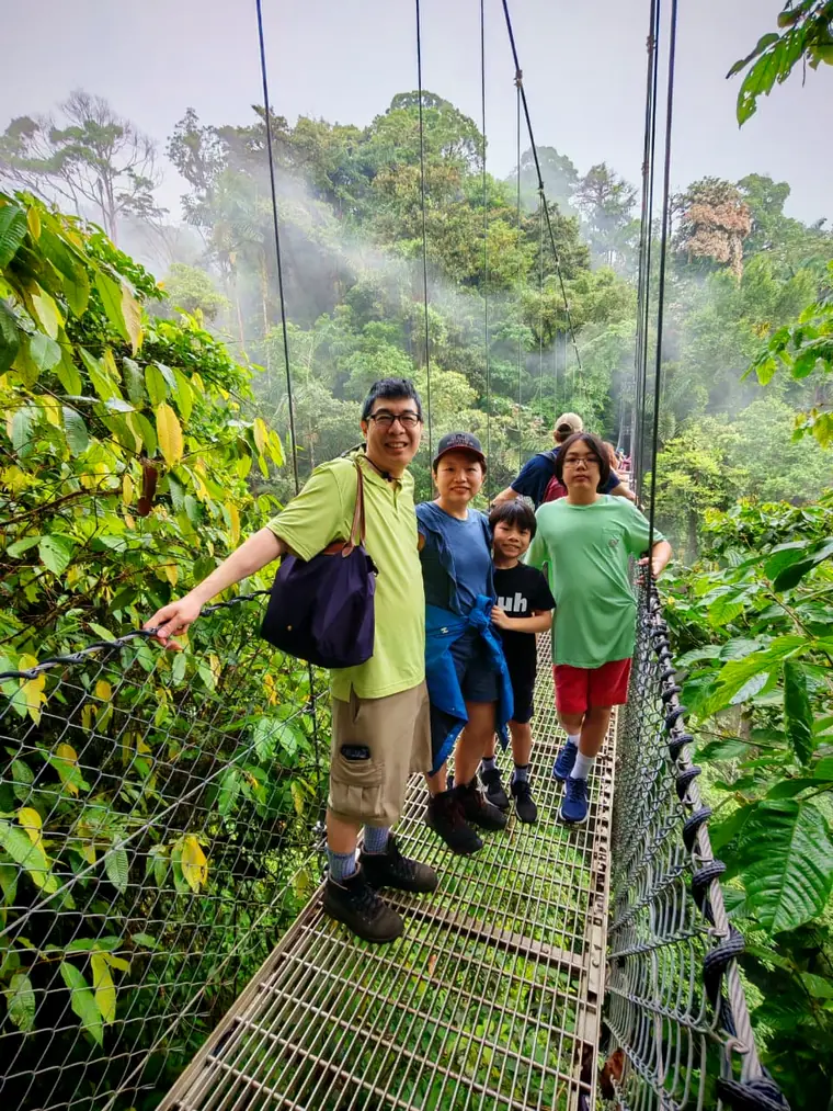 Pasajeros en un puente colgante del bosque de La Fortuna entre neblina