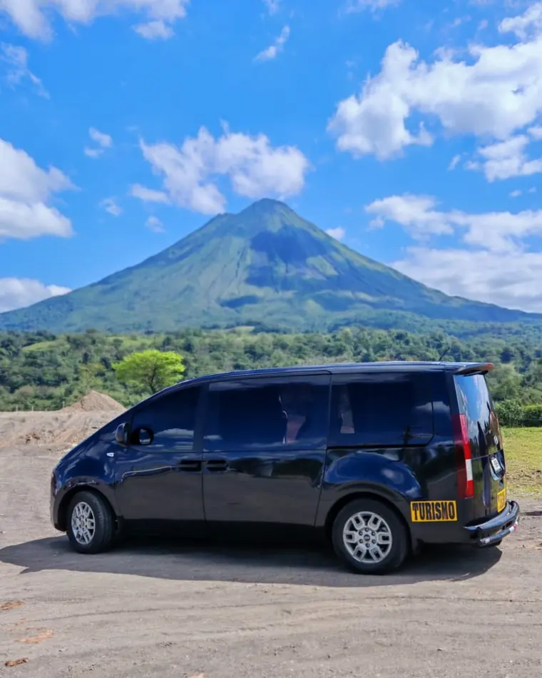 Buseta negra de turismo de Tropical Experts con el volcán Arenal de fondo